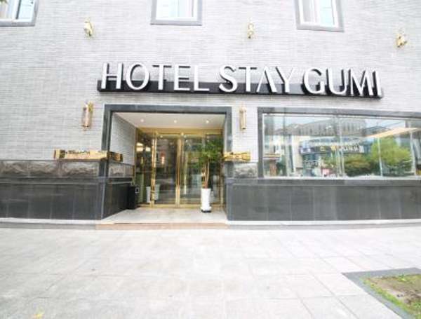 ‘HOTEL STAY GUMI’ 간판이 걸린 회색 벽돌 건물 정면과 유리문 입구